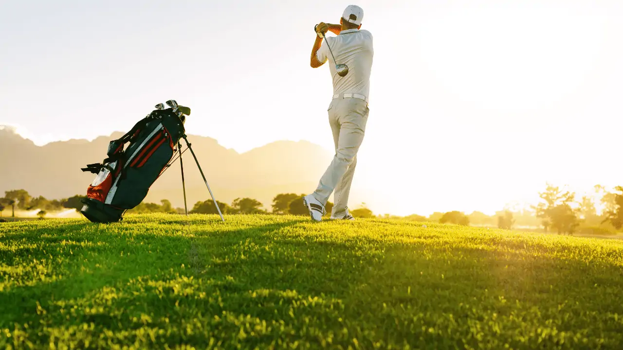 Golf photo with man hitting golf ball with his fairway wood into the sunset.