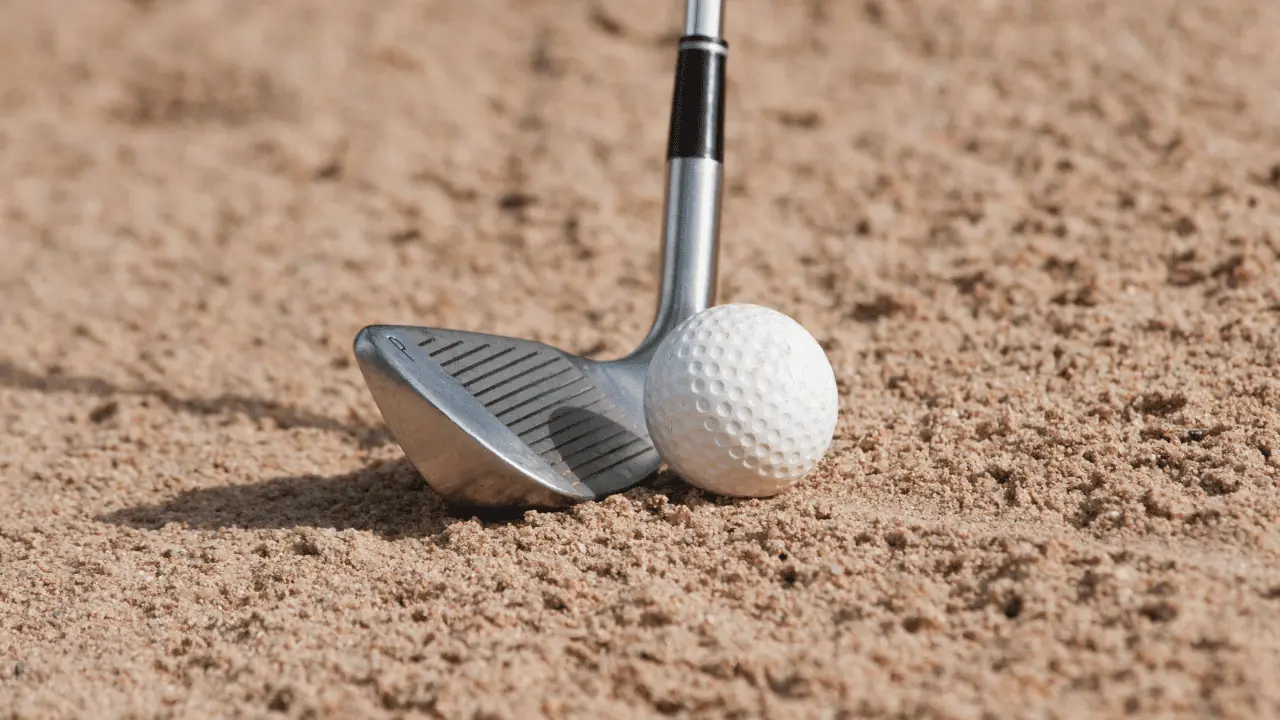 how many wedges should you carry article showing a wedge club head in the sand trap with a golf ball.