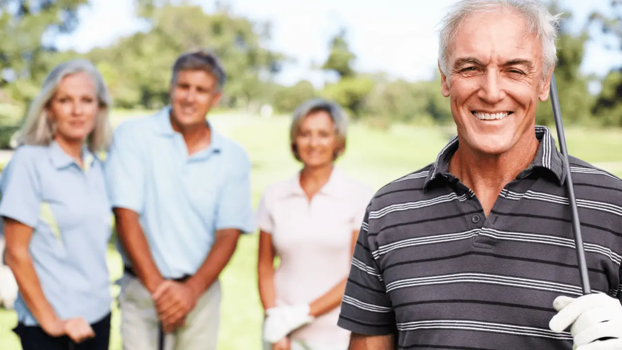 Phone of senior golfer smiling with his iron in hand with 3 people in the background. Happy golfers shown on the golf course wearing their golf gloves.