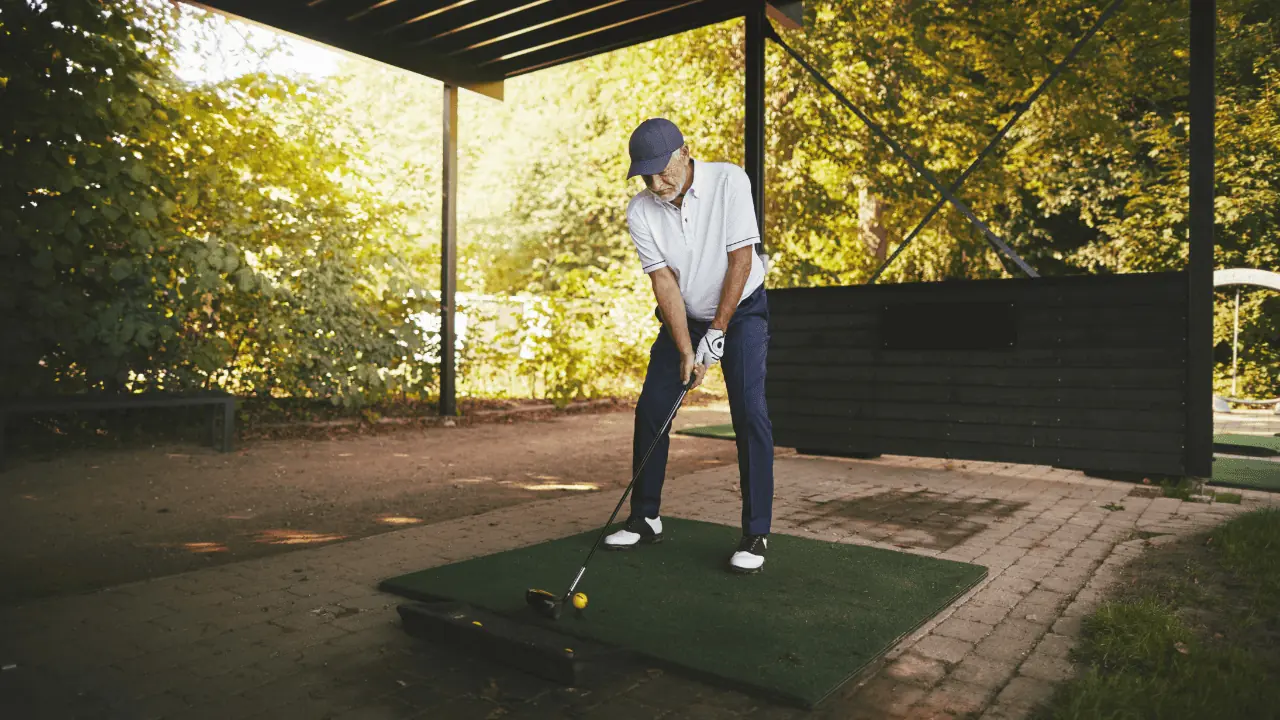outdoor golf simulator photo with senior man dressed in golf clothes hitting off a mat