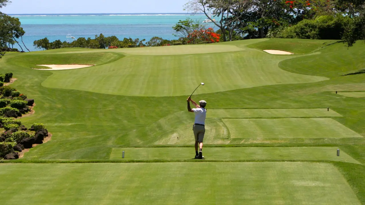 golfer hitting from the tee box with his fairway wood with the ocean behind the green.