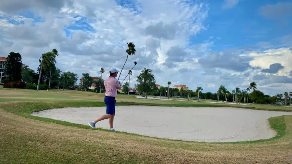 golfer hitting his 5 wood near the bunker on a golf course