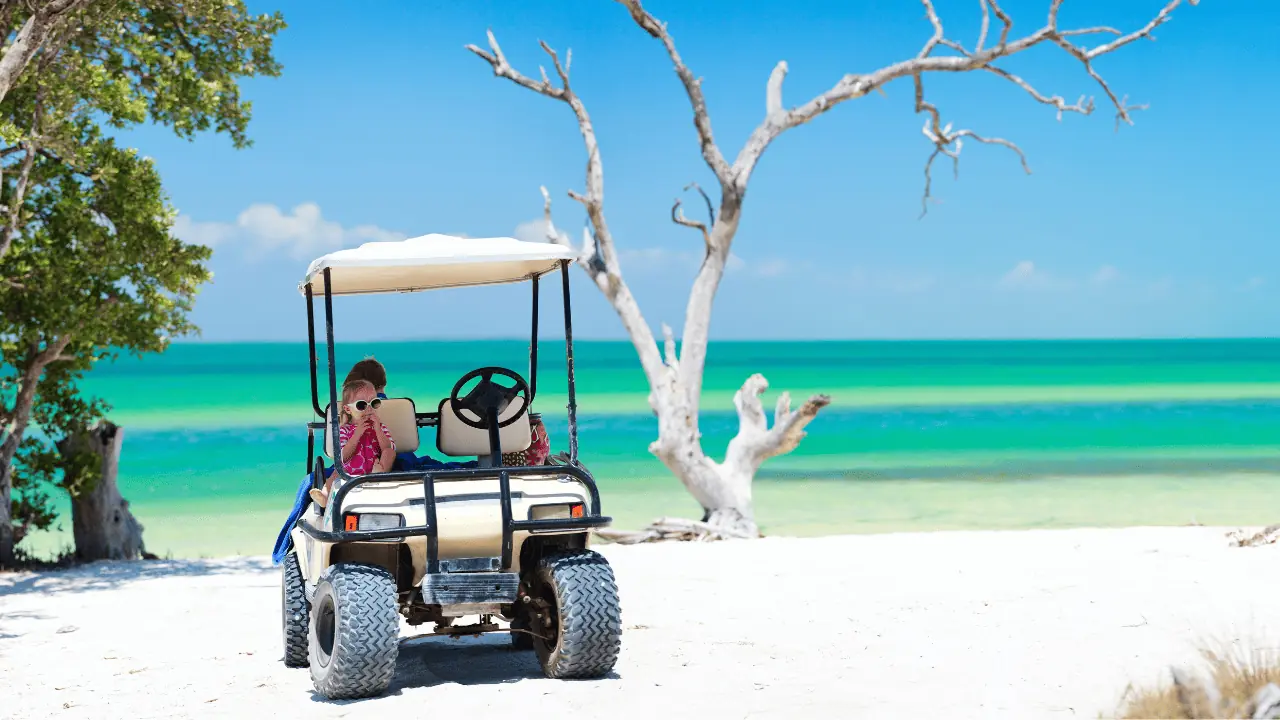 golf cart tires in the sand with a golf cart on the beach with kids sitting in itt.