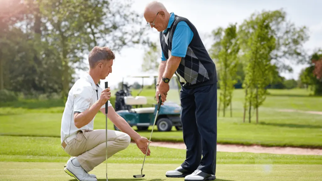 senior golfer getting putting lessons from a golf pro showing golf equipment - putters, and golf cart in the background