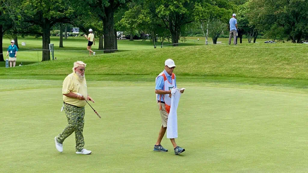 John Daly finishing his putt and walking of the green with his caddy. Known to some as the fat golfer who smokes. 