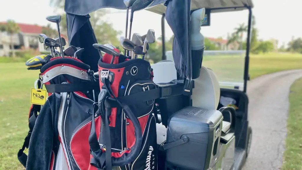 Showing two red and black golf bags on a golf cart on a golf course in the article 
How Much Do Fitted Golf Clubs Cost