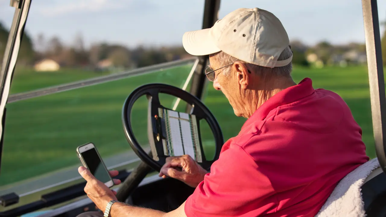 golf swing analyzer app with a senior golfer looking at it in his golf cart.