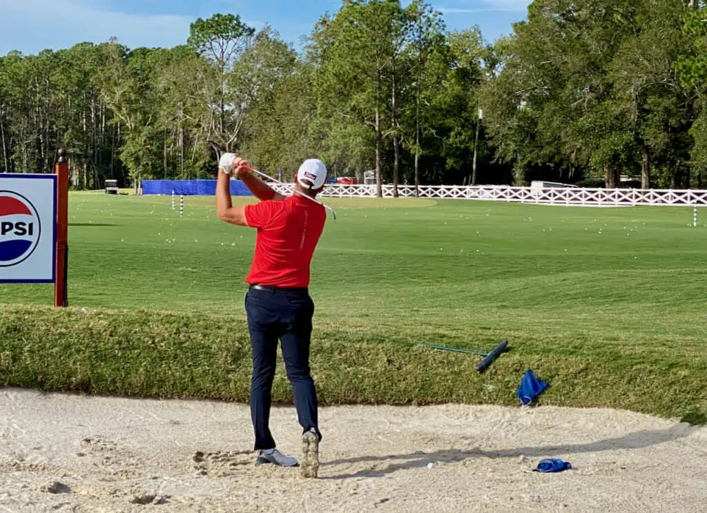 Photo of taller man hitting his golf irons from a bunker.