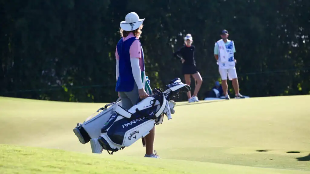 caddie carrying to golf bags across the golf course