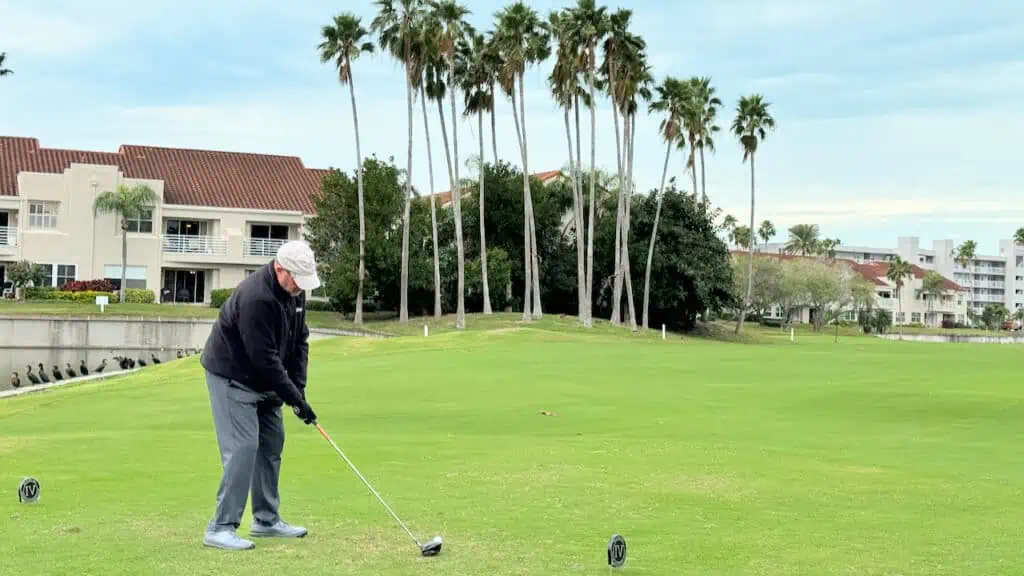 Senior golfer hitting his driver off the tee on a Florida golf course with palm trees in the distance.
