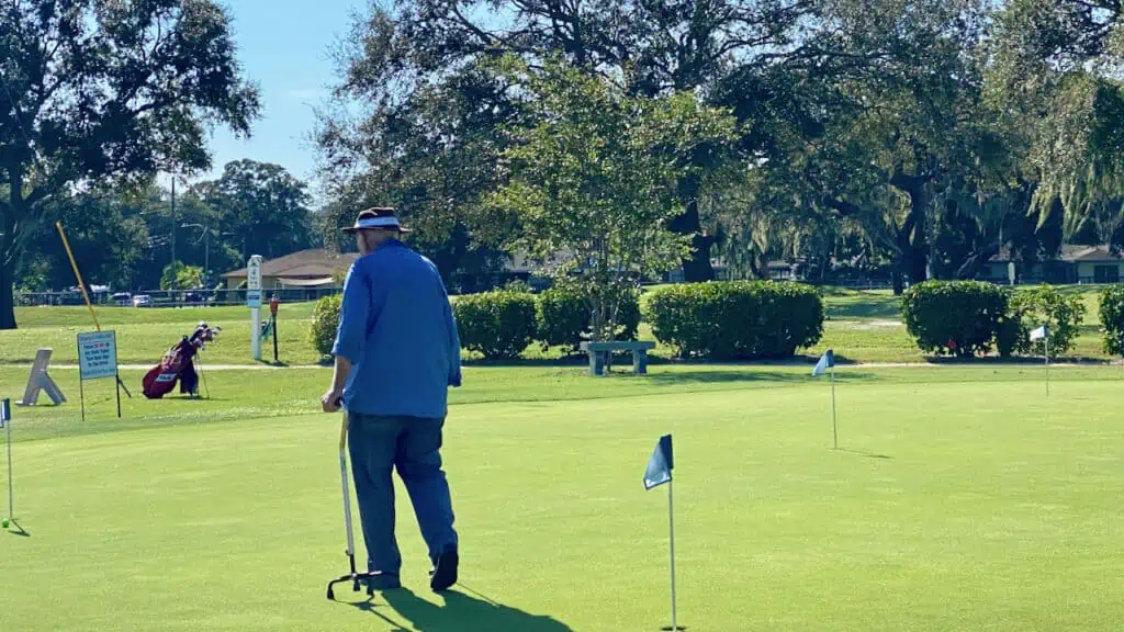 Golfer using his cane on the putting green.