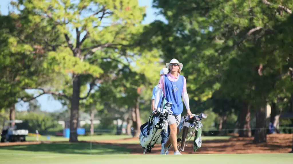 photo of a caddie carrying two bags across the green.
